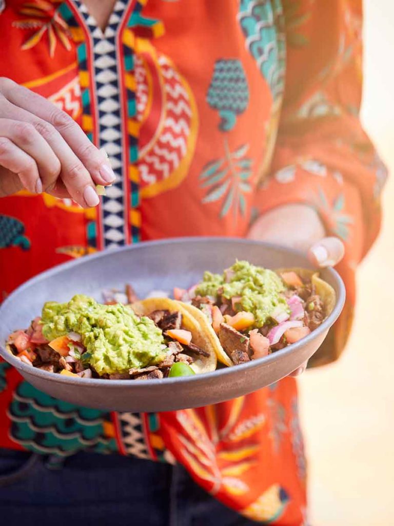 Someone holding a plate of tacos.
