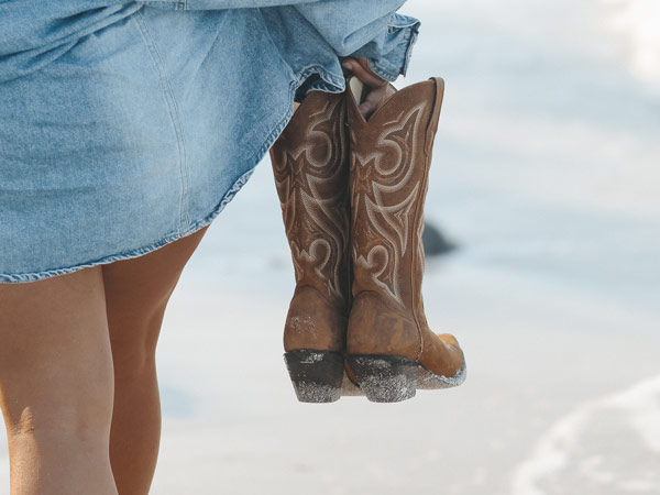 Girl Carrying Cowgirl Boots On The Beach