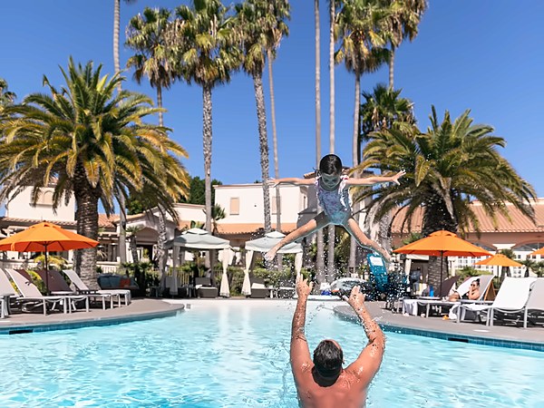 Father playfully tossing his daughter into the air in the outdoor pool surrounded by palm trees at San Diego Mission Bay Resort