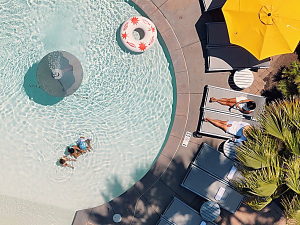 Aerial view of the resort pool at San Diego Mission Bay Resort with sunbathers on lounge chairs, a yellow umbrella, and a colorful pool float on a sunny day