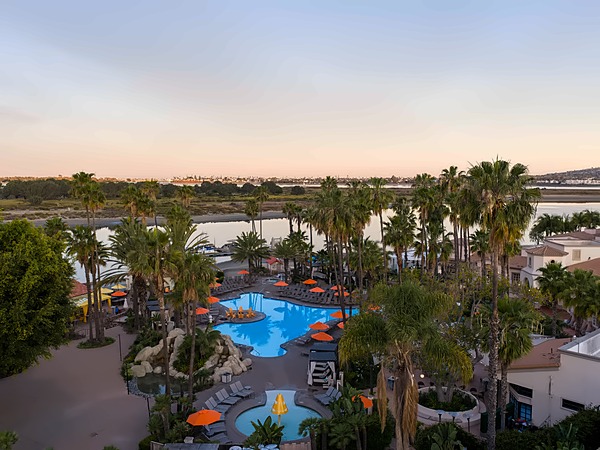 Aerial sunset view of the pool and lazy river surrounded by palm trees at San Diego Mission Bay Resort, with Mission Bay waterfront in the background