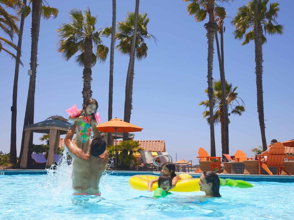 Family playing in the outdoor pool with palm trees at San Diego Mission Bay Resort