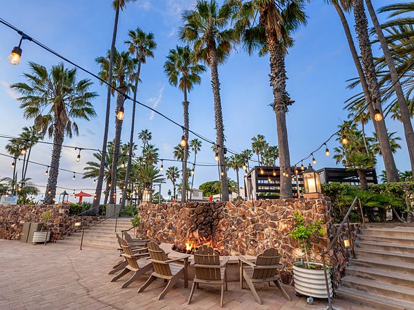 Fire pit lounge under string lights and palms at San Diego Mission Bay Resort.