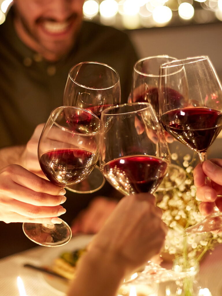 Friends clinking glasses of red wine over a candlelit holiday dinner table during Thanksgiving dining at San Diego Mission Bay Resort.